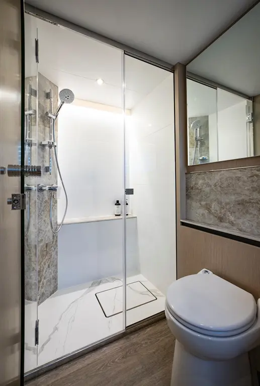 Modern bathroom featuring a shower with glass doors, rainfall showerhead, and a white toilet next to a wooden cabinet.